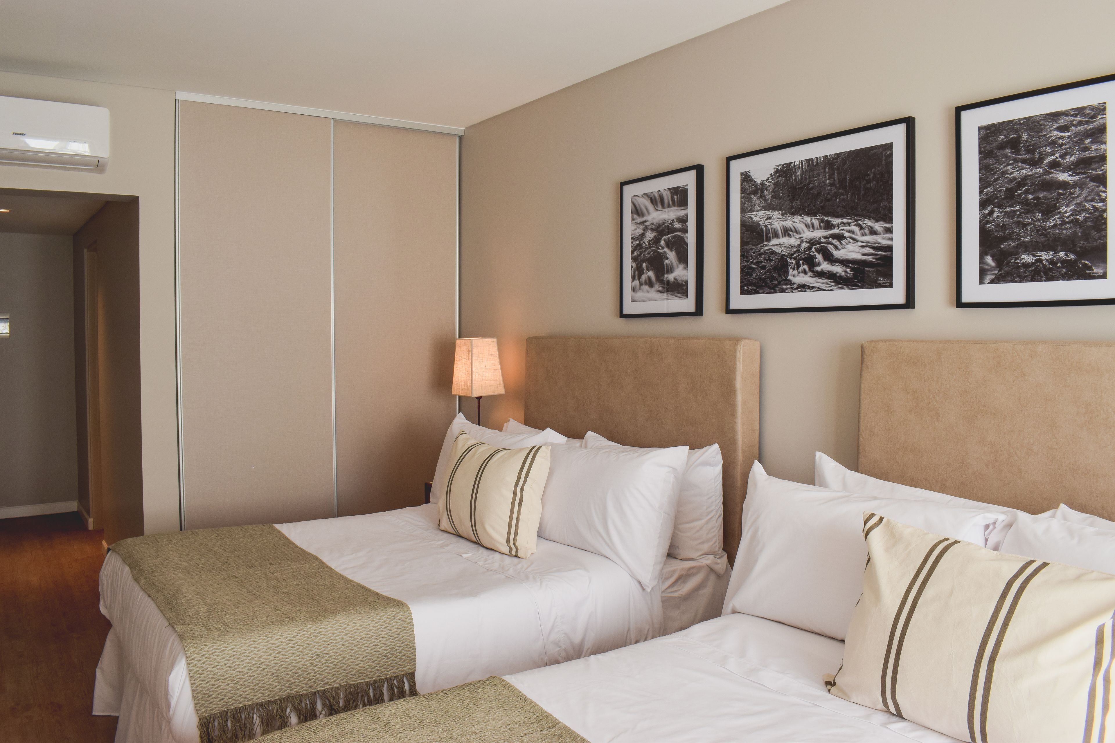 A hotel room with two beds, a wardrobe, and three framed pictures on the wall.
