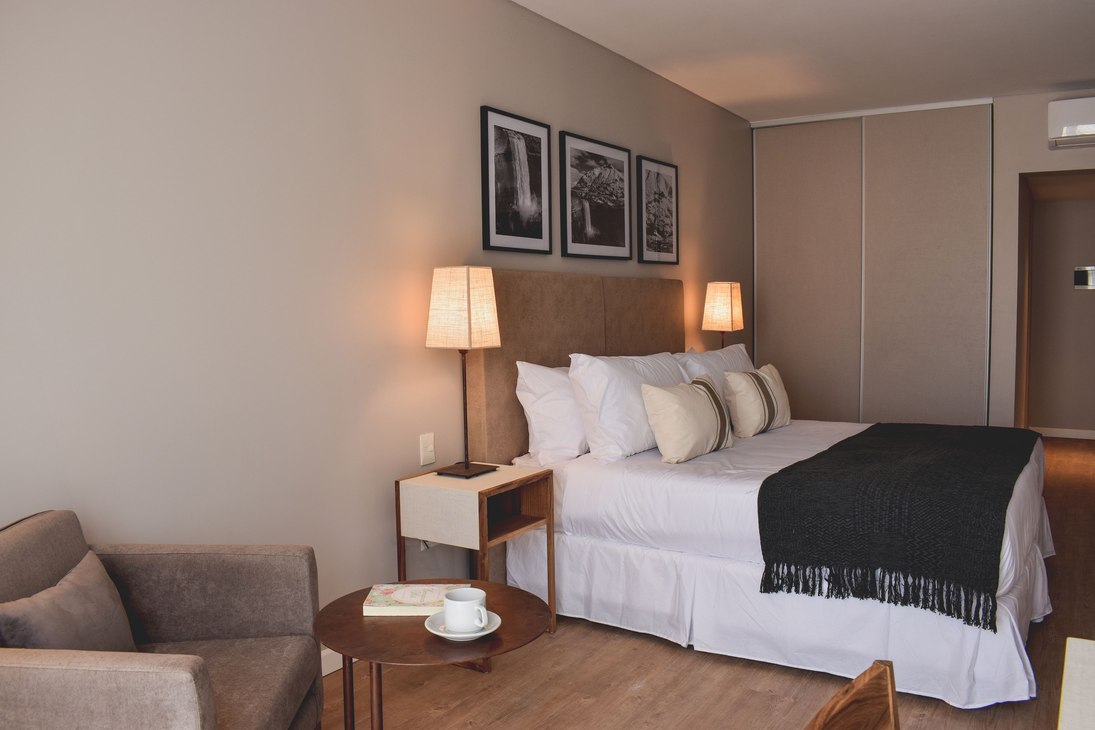 A hotel room with a bed, bedside tables, a sofa, and a small table with a cup and a book.