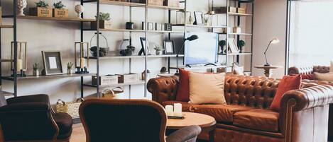 A living room with a brown leather sofa, two armchairs, a coffee table, and a bookshelf filled with various items.