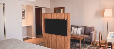 Una habitación de hotel con cama, televisión montada en un panel de madera, sofá, mesa de centro y escritorio con silla.