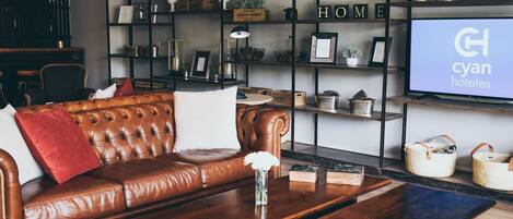 Una sala de estar moderna con un sofá de cuero, una mesa de centro de madera y una estantería llena de objetos decorativos y un televisor que muestra 'cyan hotels'.