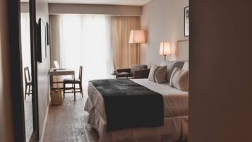 Habitación de hotel con cama, lámparas de noche, escritorio con silla, una computadora portátil y ventana con cortinas.