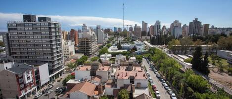 Un paisaje urbano que muestra una mezcla de edificios altos y bajos, cielo despejado, y una calle bordeada de árboles y coches estacionados.
