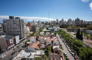 A cityscape with a mix of high-rise and low-rise buildings, a clear sky, and a street lined with parked cars and trees. - Cyan Soho Neuquen Hotel (Neuquén)