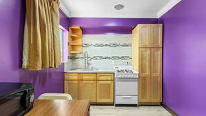 Cocina compacta con armarios de madera, estufa blanca y pared morada.