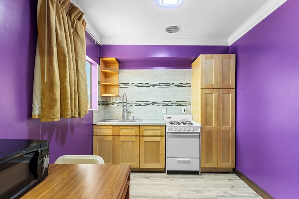 A compact kitchen with wooden cabinets, a white stove, and a purple wall.