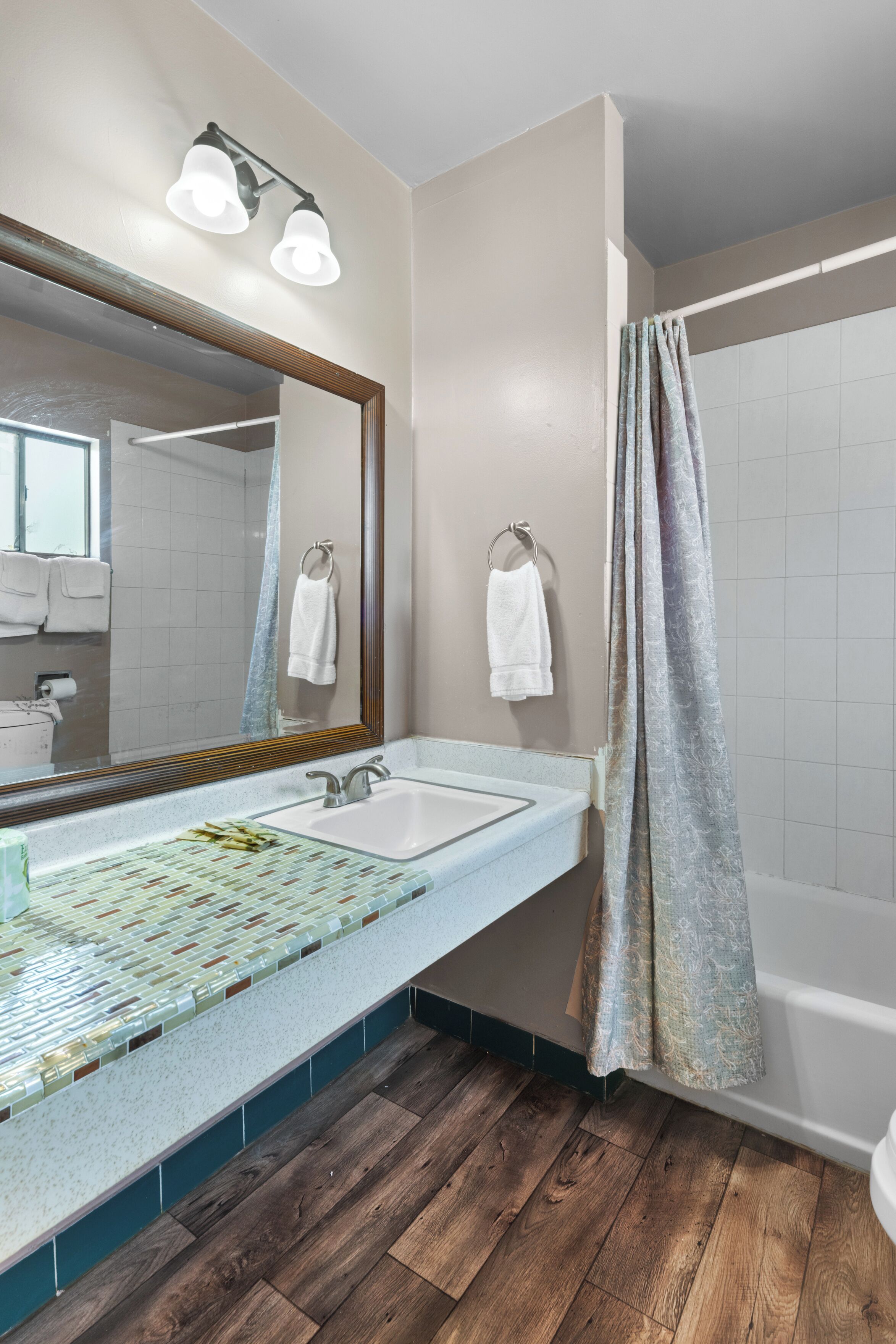 A bathroom with a wooden floor, a sink with a mirror, and a shower curtain.