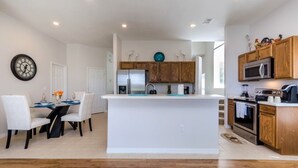 Cocina moderna con armarios blancos, una isla central y un comedor con sillas blancas.