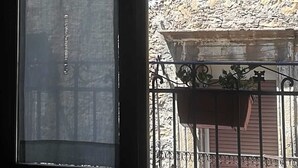 A window with a decorative metal grille and a view of a stone building with a window and balcony. - L'Angolo sulla Piazza (Mirabella Imbaccari)
