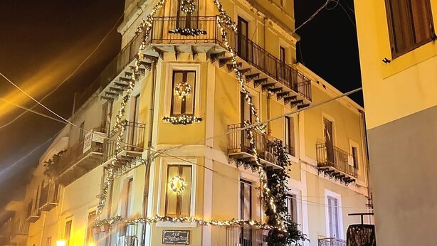 A multi-story building with balconies, decorated with lights and wreaths, suggesting a festive season. - L'Angolo sulla Piazza (Mirabella Imbaccari)