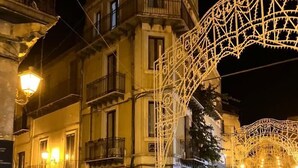 A street with buildings, a covered outdoor seating area, and a decorative light structure. - L'Angolo sulla Piazza (Mirabella Imbaccari)