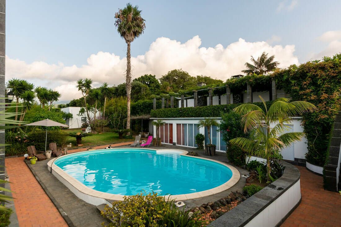 A swimming pool surrounded by lush greenery and a building with a white facade.