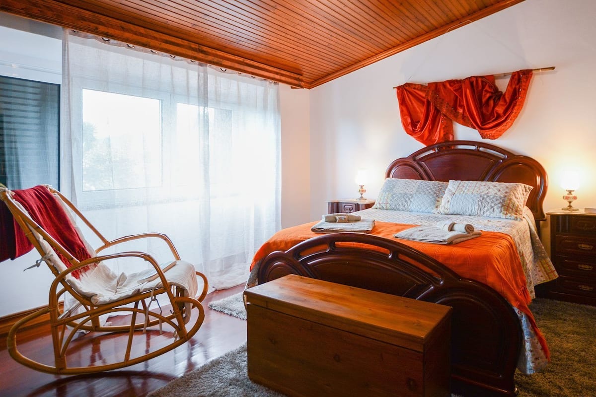 Een slaapkamer met een houten bed, een schommelstoel, een nachtkastje en een dressoir.