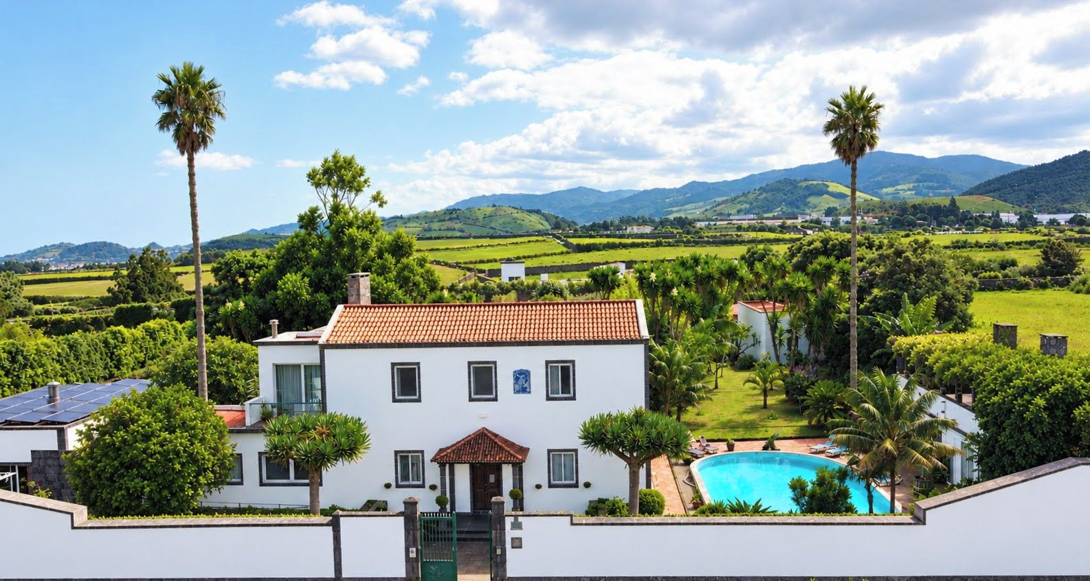 A white building with a red-tiled roof, a swimming pool, and palm trees.
