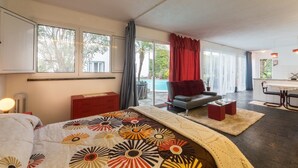 A modern hotel room with a large bed, a sofa, a dining area, and a view of a pool. - Quinta Minuvida Orchard Lodge (Ribeira Grande)