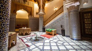 A richly decorated interior with intricate tile work, a central fountain, and a staircase with ornate railings. - Riad Al Fassia Palace (Fes)