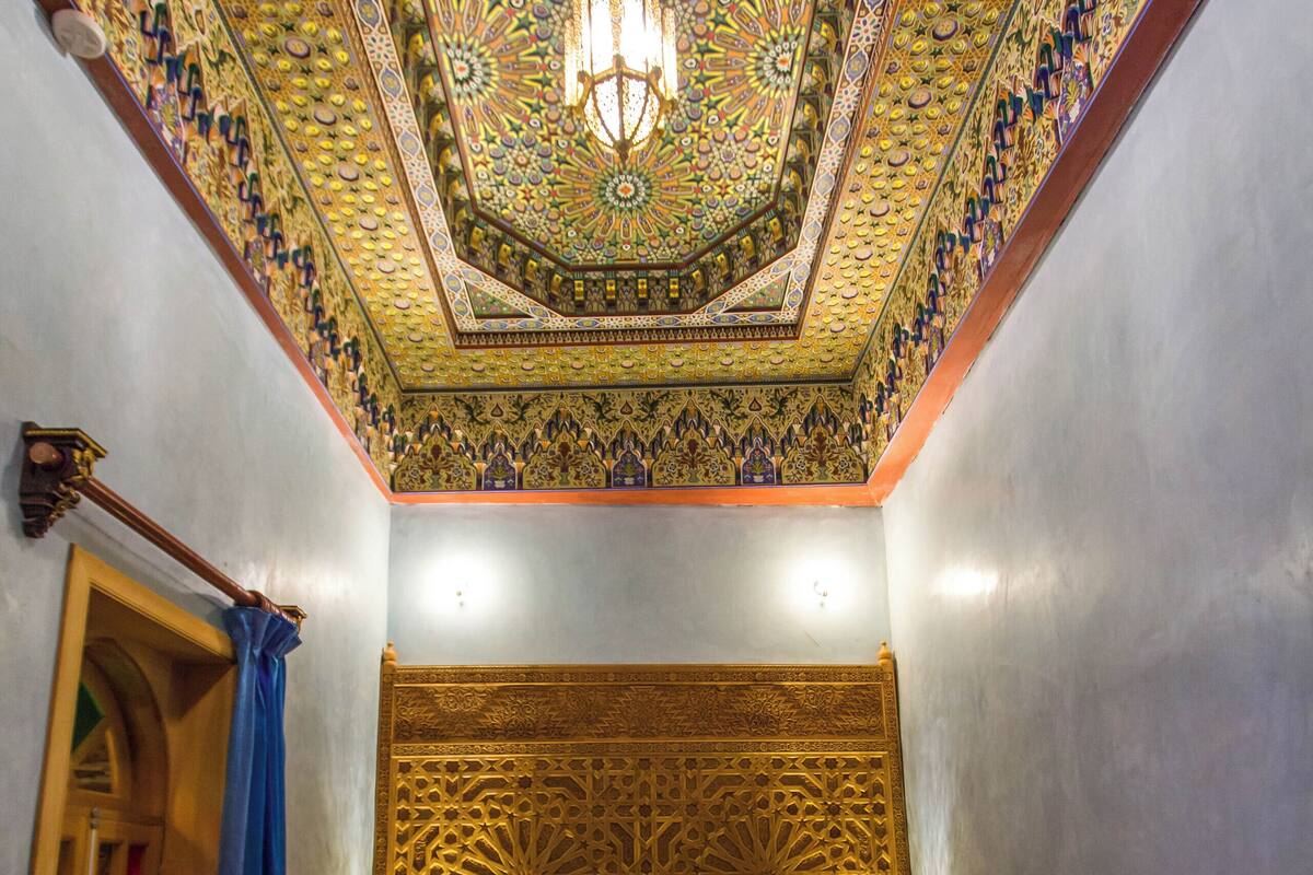 Quarto com teto estampado, cama com cabeceira de madeira e mesa de cabeceira com abajur.