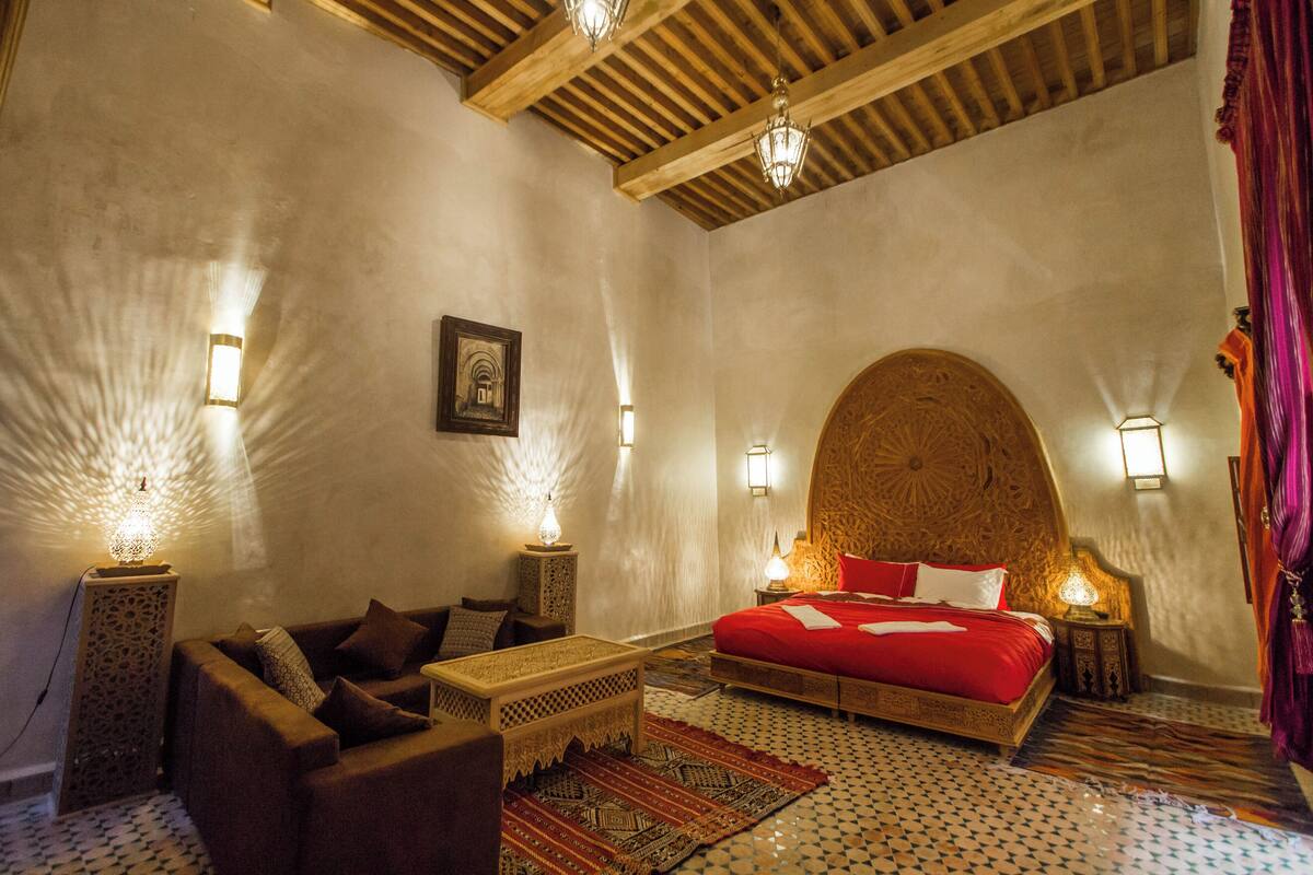 Quarto tradicional marroquino com uma cama grande, um sofá e um tapete estampado.