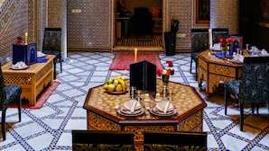 A traditional Moroccan interior with intricate tile work, a central dining area with a table set for four, and a staircase with wooden railings. - Riad Al Fassia Palace (Fes)