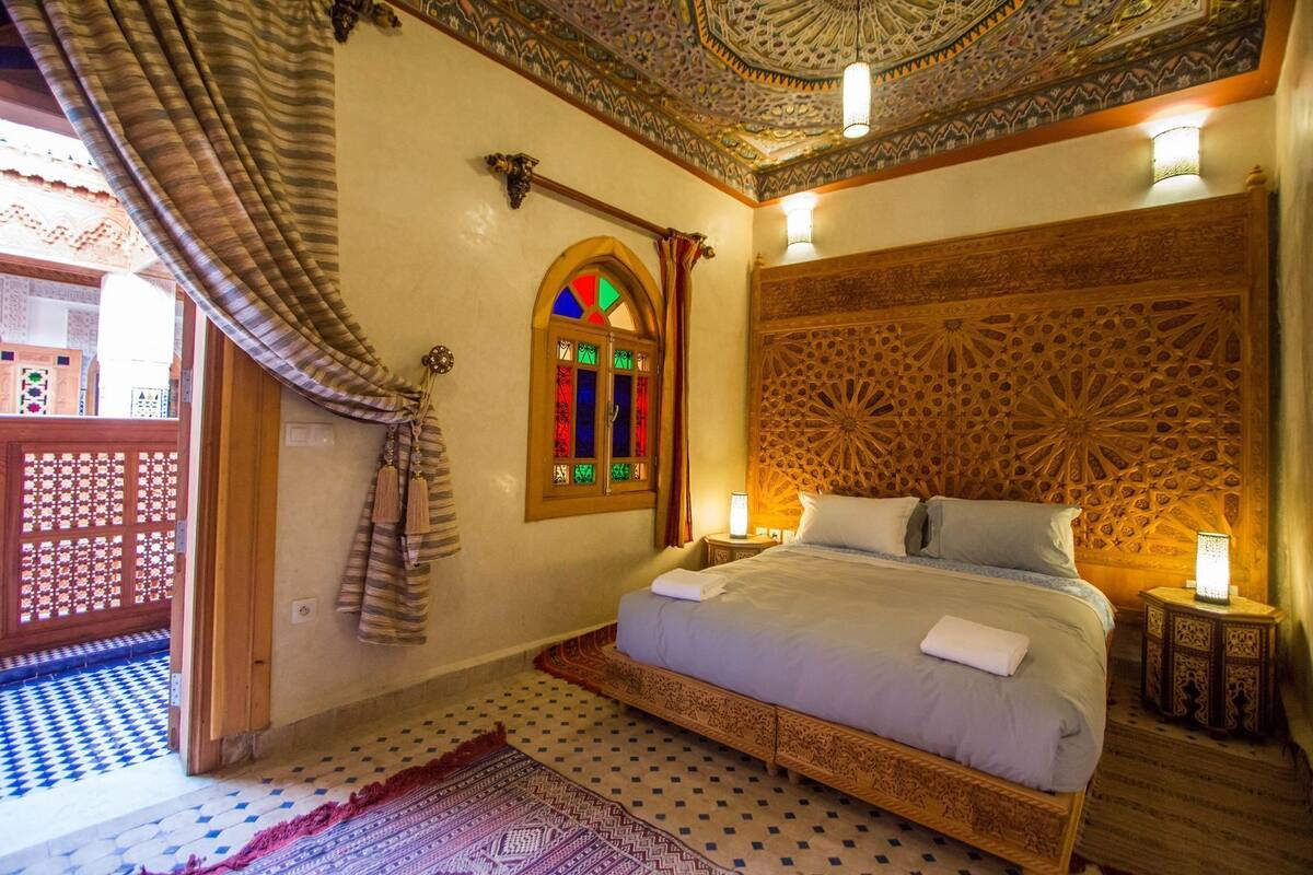Quarto com cama, parede decorativa, janela com vitrais e piso estampado.
