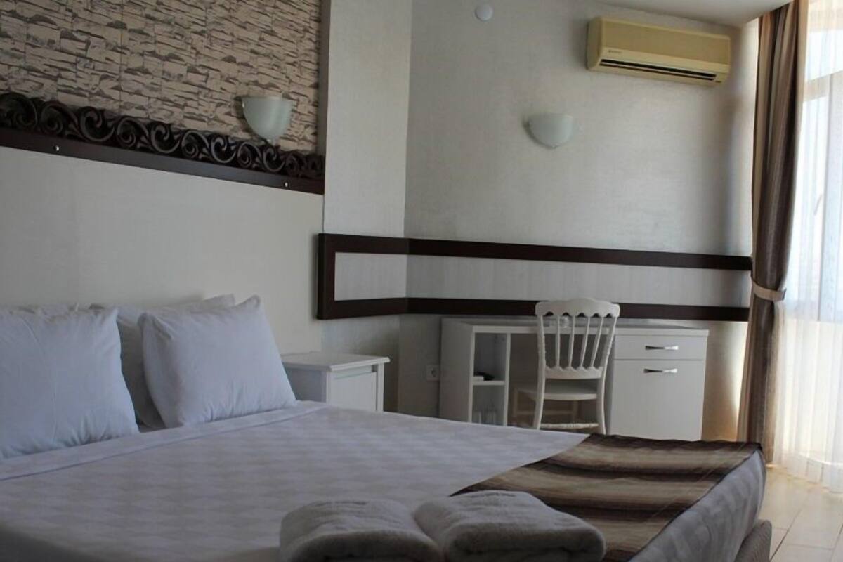 Una habitación de hotel con cama, escritorio, silla y ventana con cortinas.