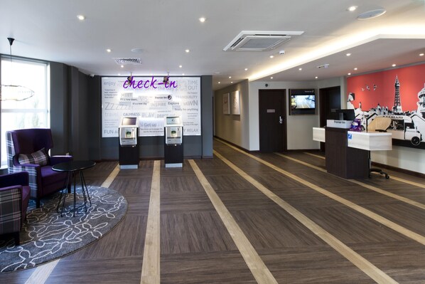 A hotel lobby with a reception desk, check-in counters, a seating area with a sofa and chairs, and a large wall with motivational phrases. - Premier Inn Bridlington Seafront (Bridlington)