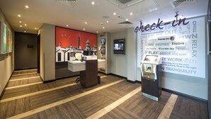 A hotel reception area with a check-in counter, a digital screen, and a wall with inspirational words. - Premier Inn Bude (Bude)