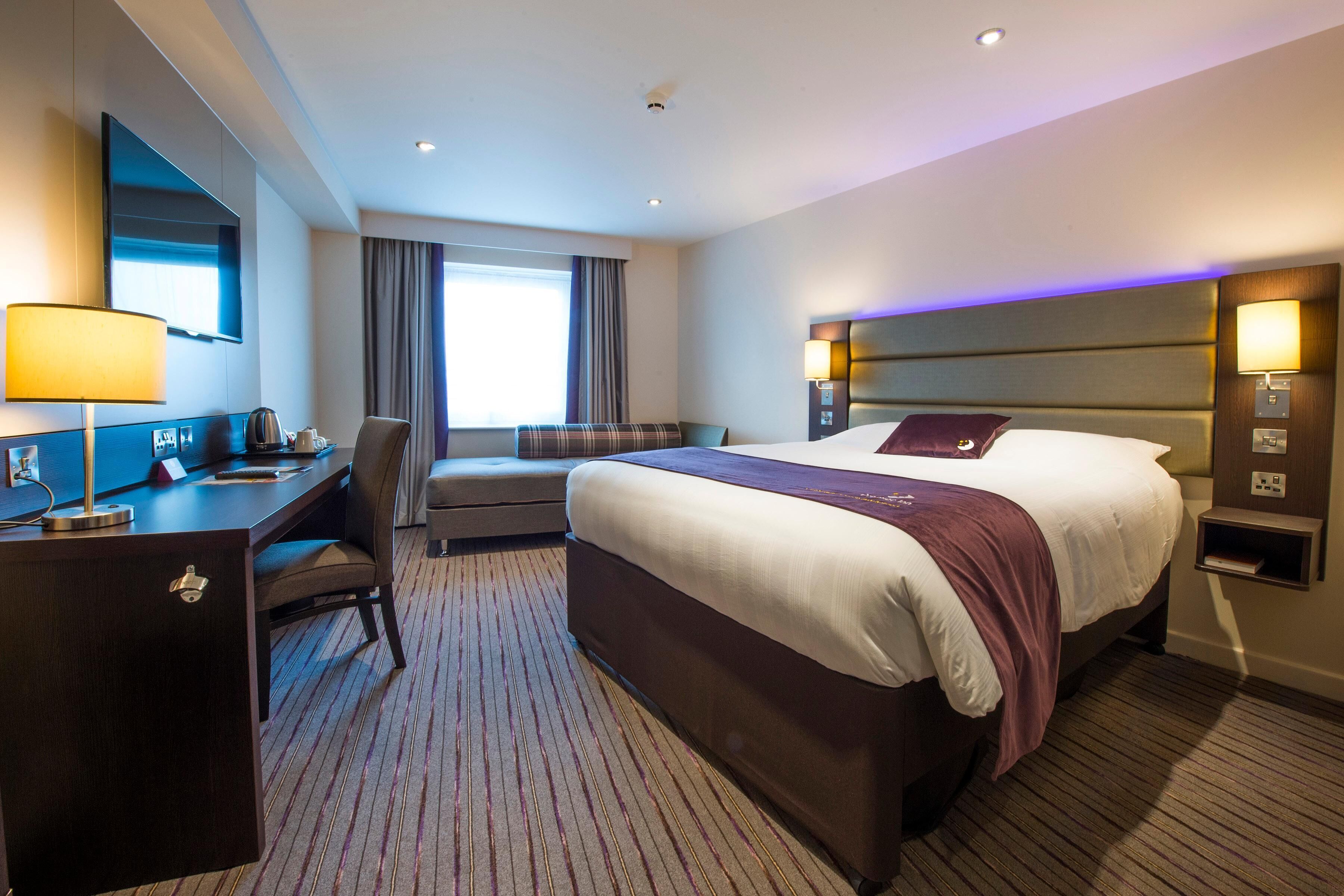 A hotel room with a large bed, a desk, a chair, a TV, and a window.