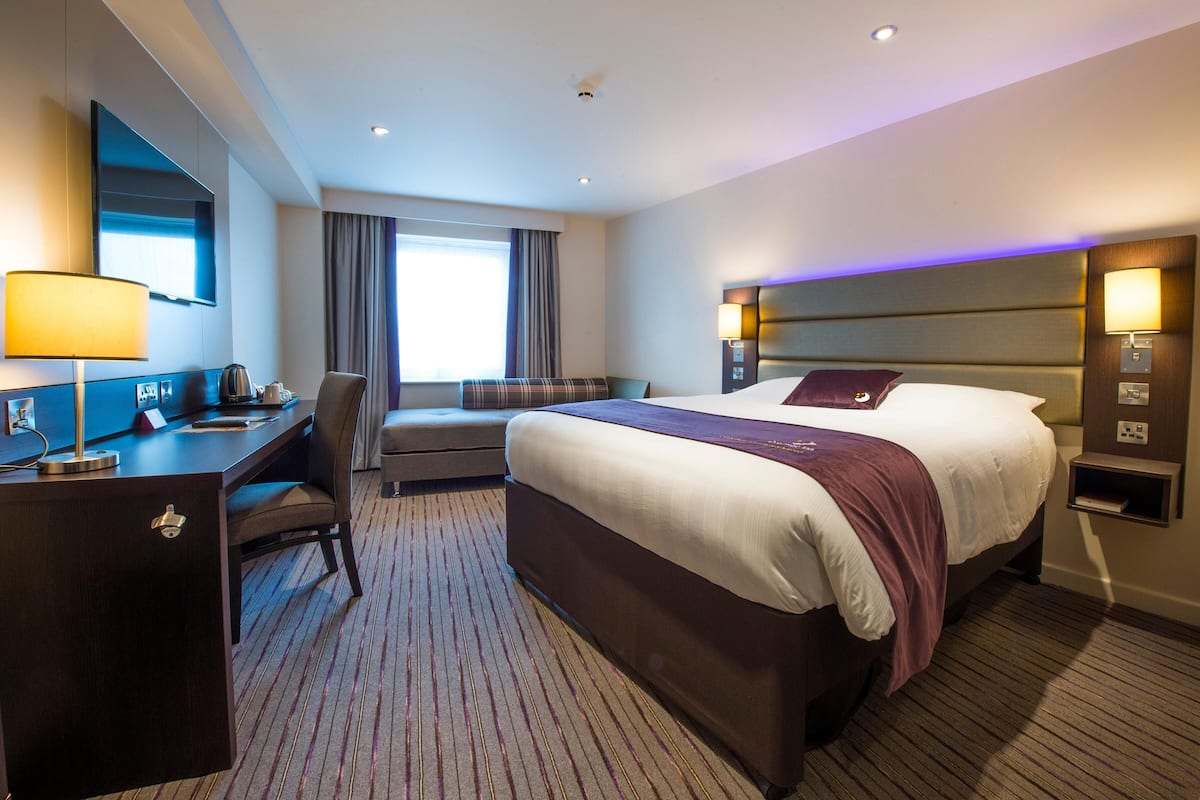 A hotel room with a large bed, a desk, a chair, a TV, and a window.