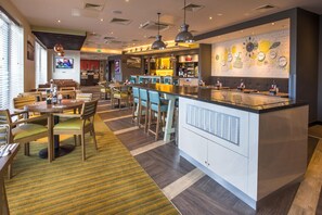 A modern restaurant with a bar area, seating arrangements, and a television screen. - Premier Inn Bude (Bude)