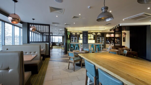 A modern restaurant interior with booths, a bar area, and a seating arrangement. - Premier Inn Leeds Headingley (Leeds)