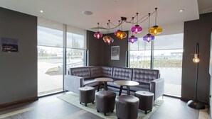 A modern lounge area with a sectional sofa, round tables, and ottomans. - Premier Inn Slough West - Slough Trading Estate (Slough)