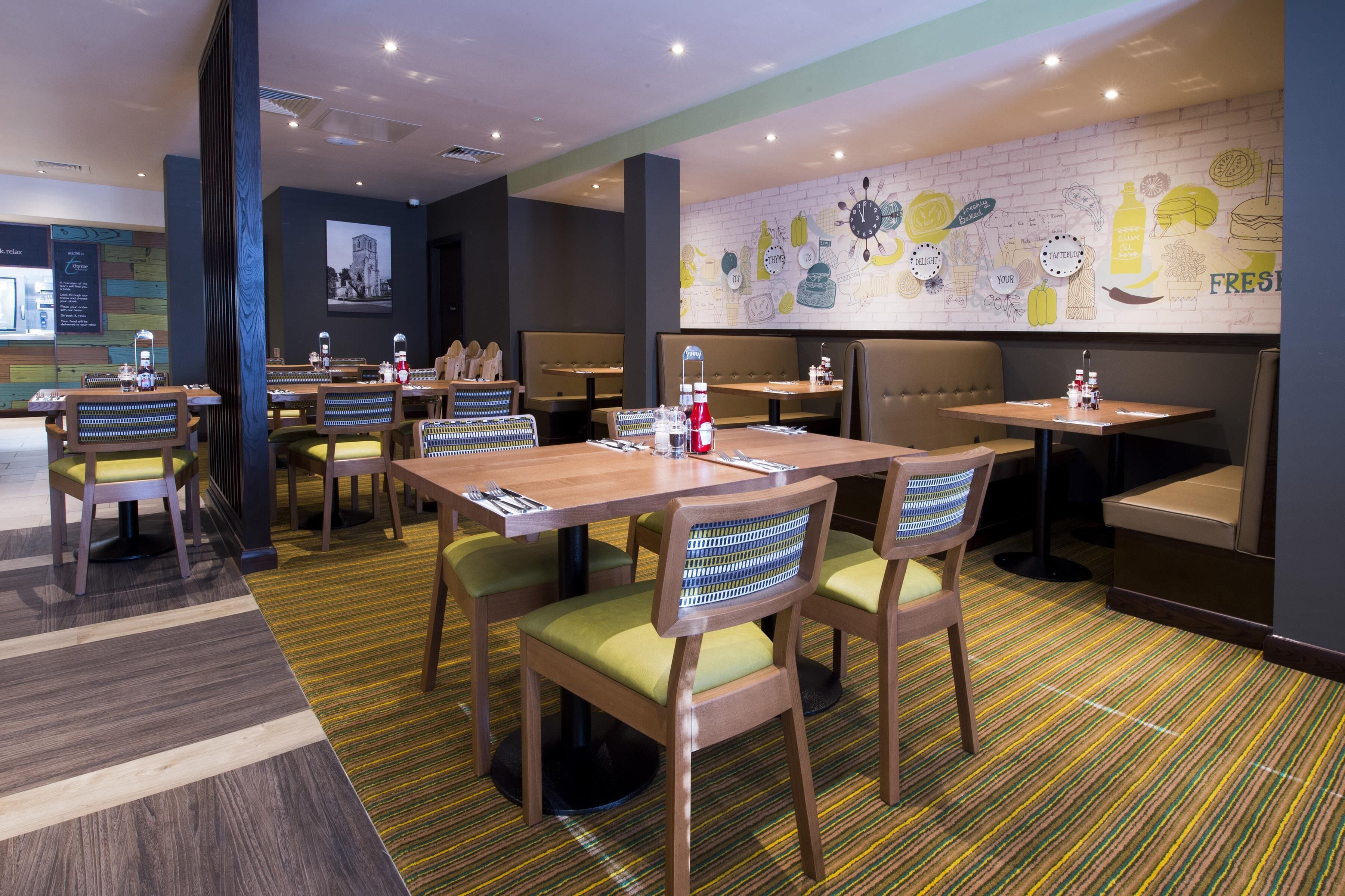 Un restaurant avec des banquettes et des tables, des chaises rembourrées de couleur verte et une fresque murale illustrant des plats.
