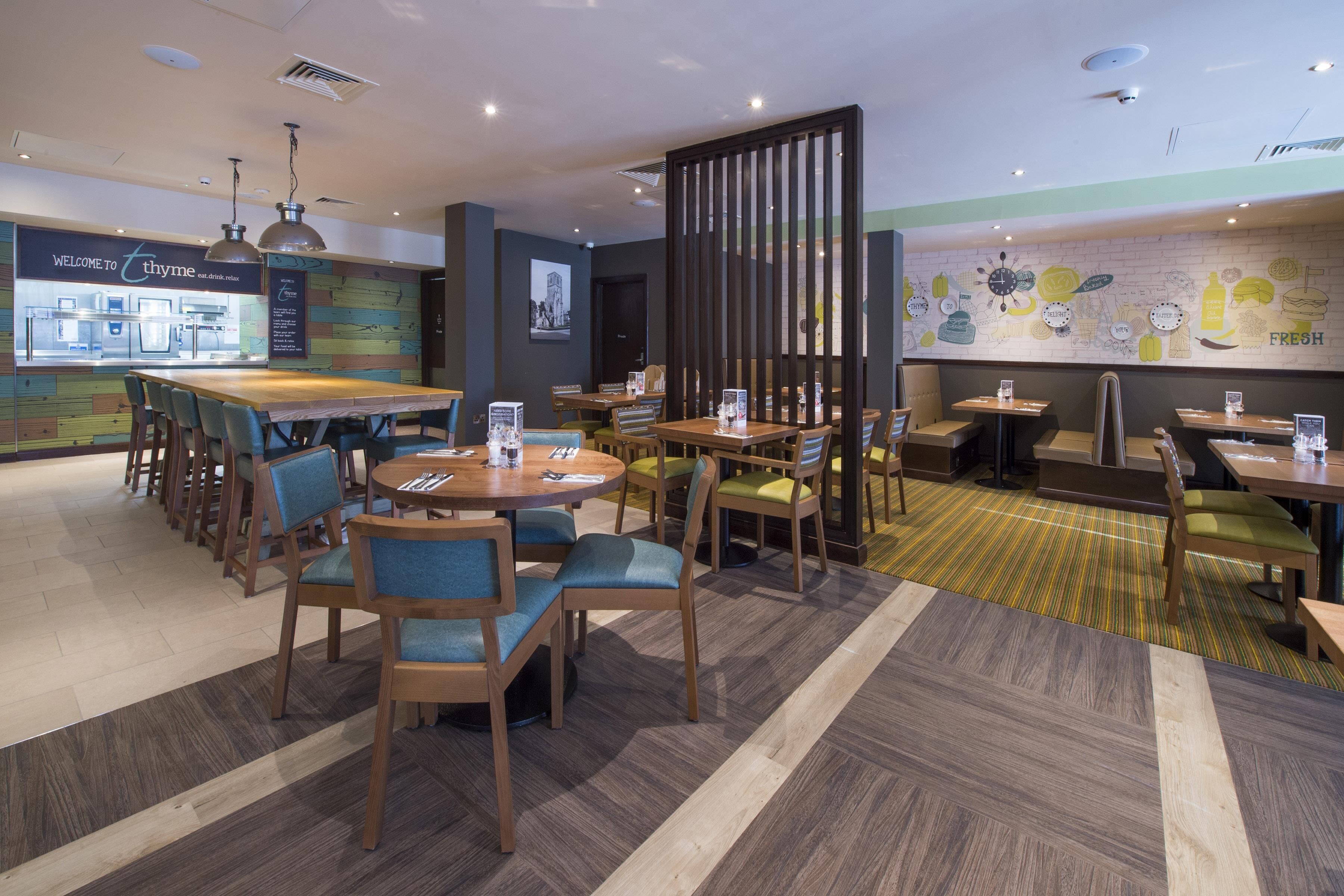 Un restaurante con zona de bar, diversas opciones de asientos y una pared con ilustraciones de comida.