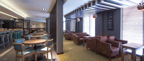 A modern hotel lobby with a bar area, seating arrangements, and a patterned carpet.