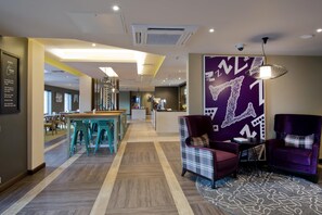 Un hall de hotel con mostrador de recepción, zona de estar y una pared con diseño.