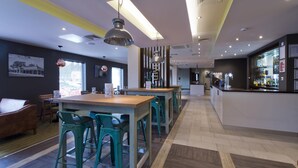 A modern bar area with a long counter, bar stools, and a visible bar stocked with bottles. - Premier Inn Ulverston (Ulverston)