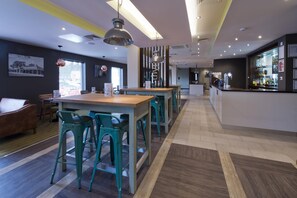 A modern bar area with a long counter, bar stools, and a visible bar stocked with bottles. - Premier Inn Ulverston (Ulverston)