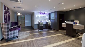 A hotel reception area with a check-in counter, a seating area with a plaid chair, a purple armchair, and a wall with motivational words. - Premier Inn Ulverston (Ulverston)