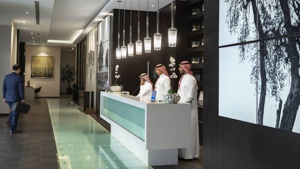 A modern hotel lobby with a reception desk, a long glass partition, and a large wall-mounted artwork.