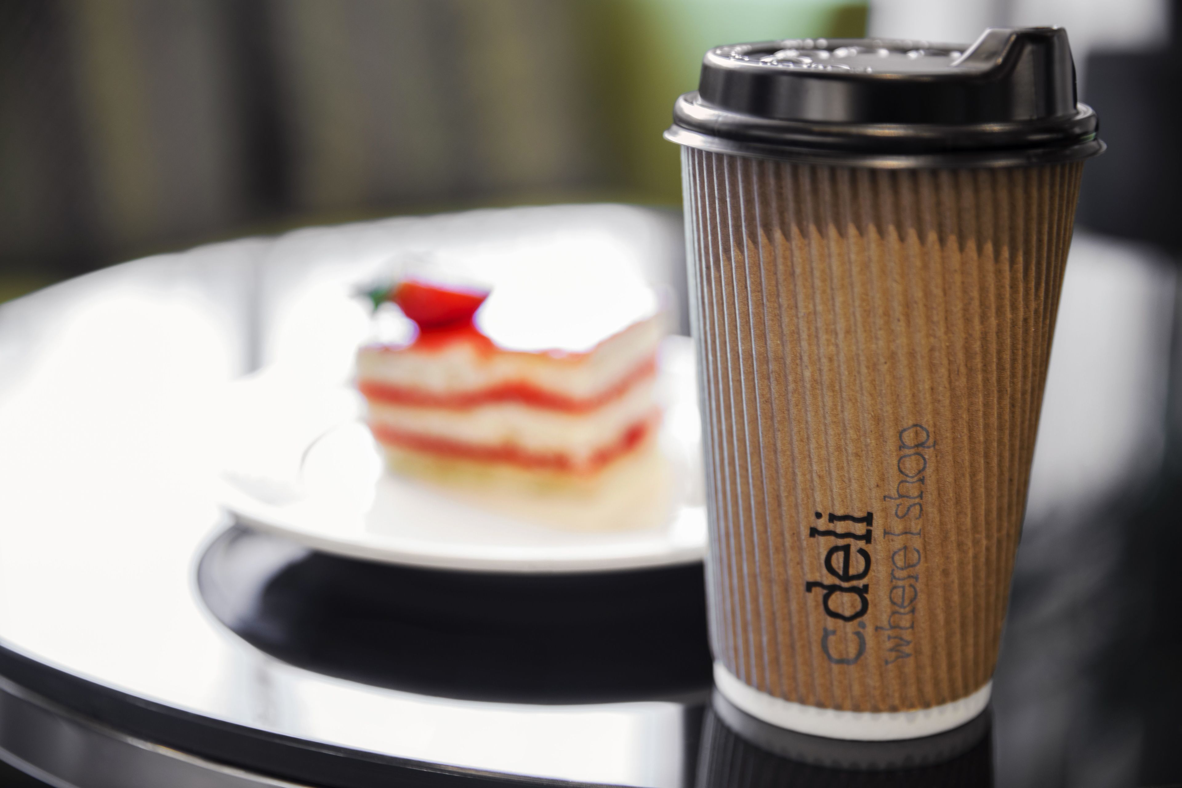 A coffee cup with a ribbed design and text on it, placed on a table with a blurred background.