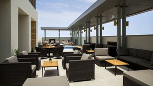 A rooftop lounge with outdoor seating, a pool, and a view of the city skyline.