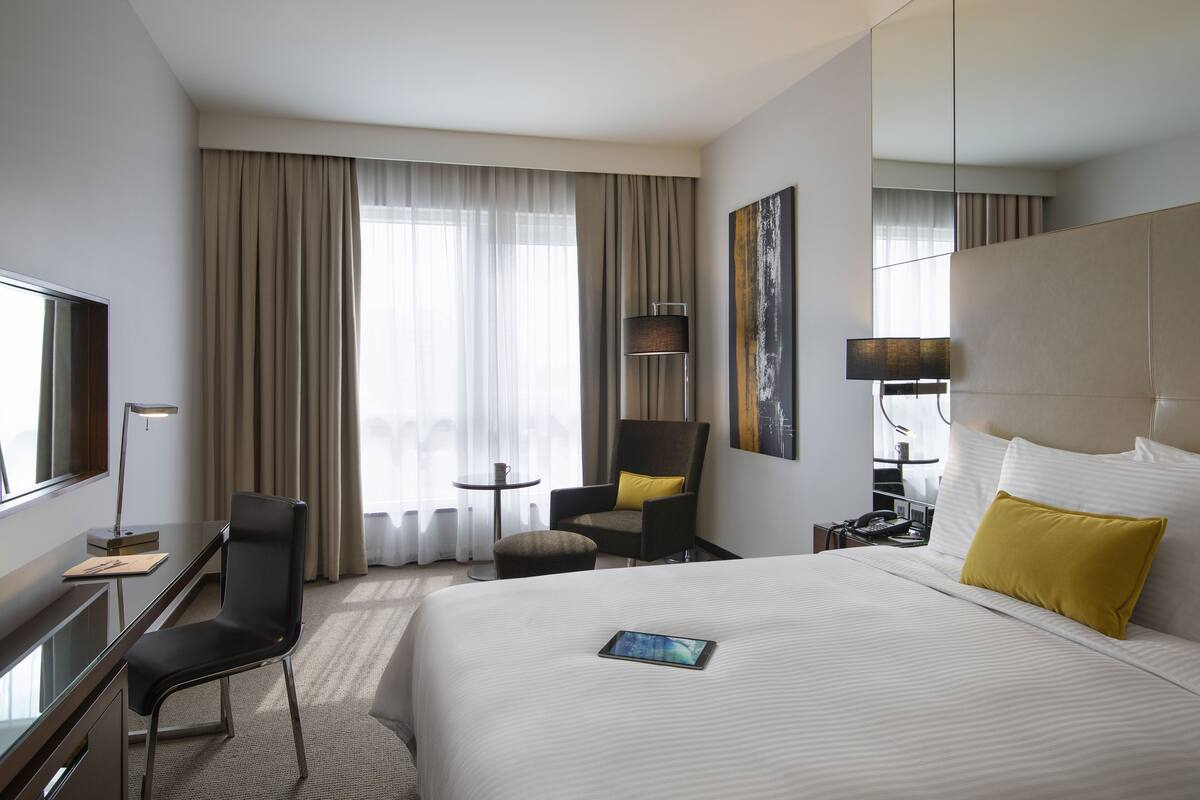 Habitación de hotel con cama, escritorio, silla, lámpara, mesita de noche y televisor.
