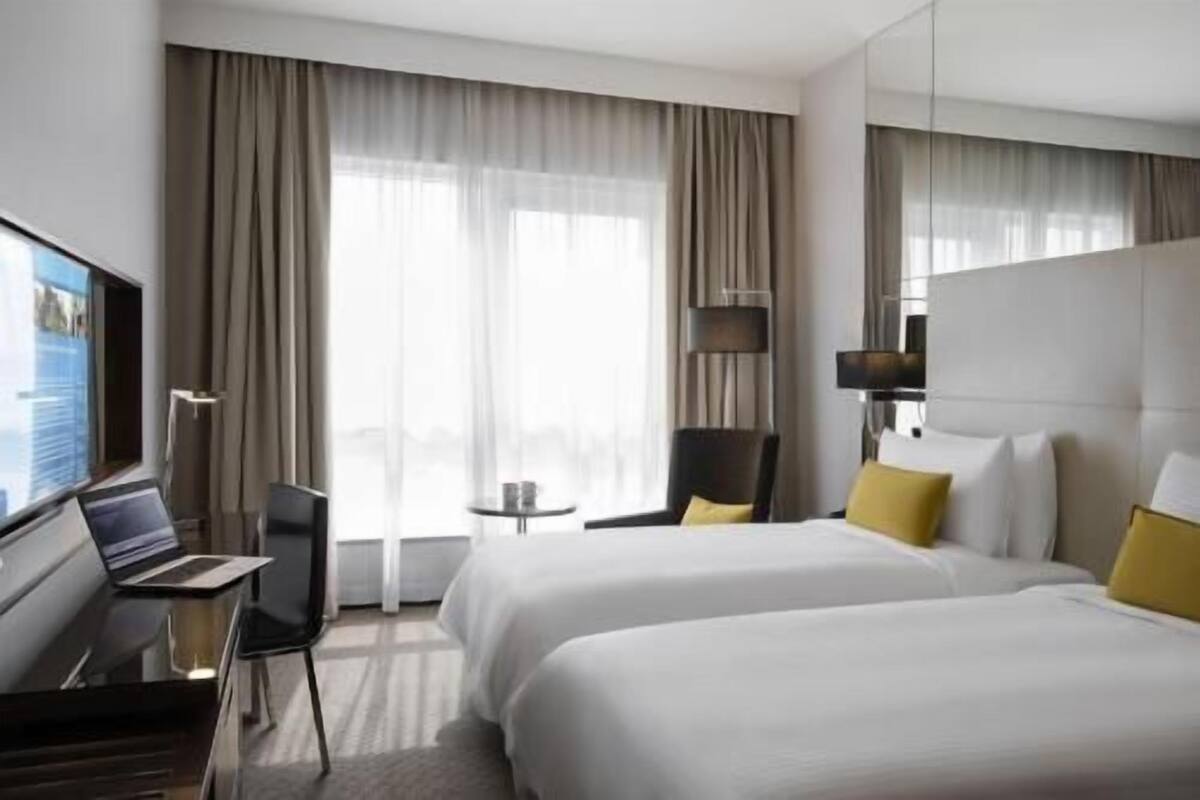 Una habitación de hotel con dos camas, un escritorio con una computadora portátil, una silla, una mesita y un televisor.