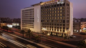 A multi-story hotel with a modern design, featuring a prominent entrance and a rooftop terrace.