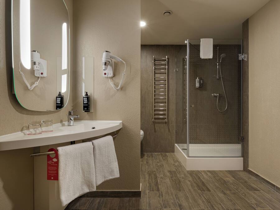 A modern bathroom with a sink, mirror, hairdryer, and shower.
