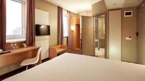 A hotel room with a bed, a desk with a chair, a television, a shower area, and a wardrobe. - ibis Kyiv Railway Station (Kyiv)