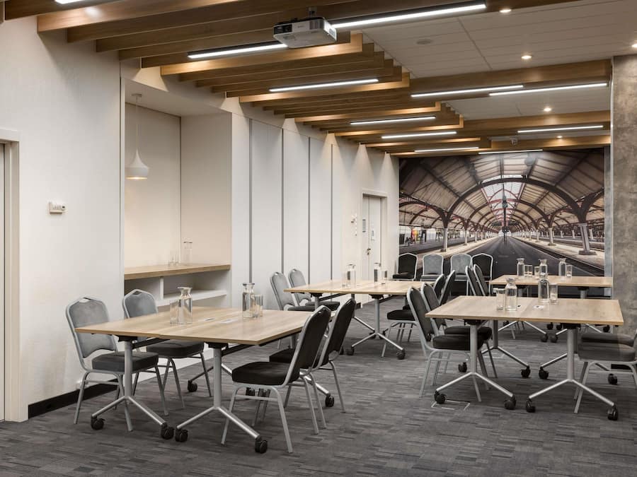 A conference room with tables and chairs, a projector, and a large mural of a train station.