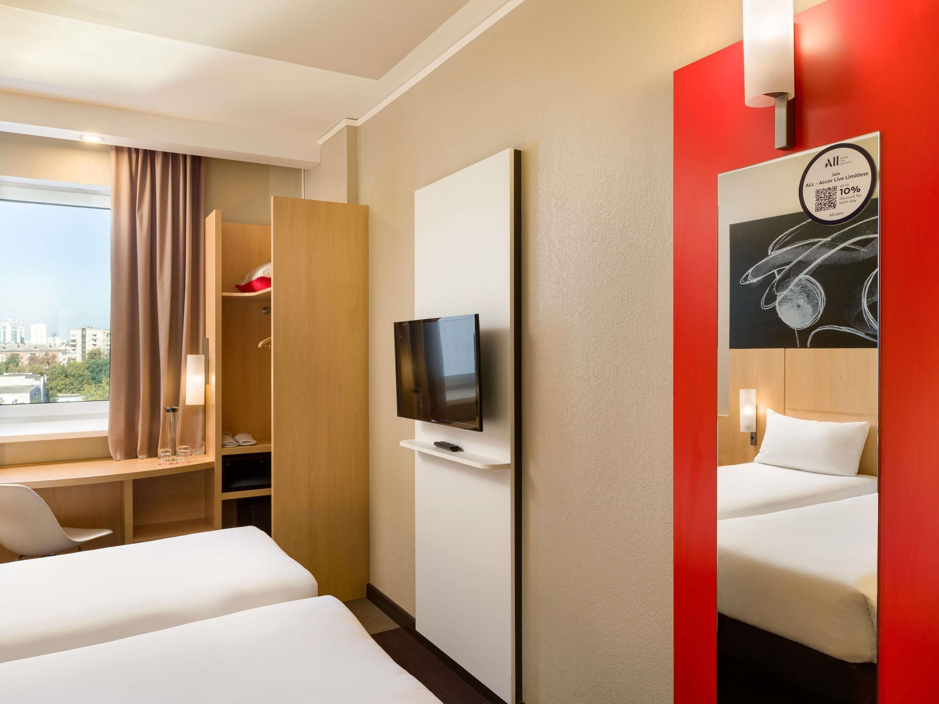 Une chambre d’hôtel avec deux lits, une télévision, une armoire et une fenêtre avec des rideaux.
