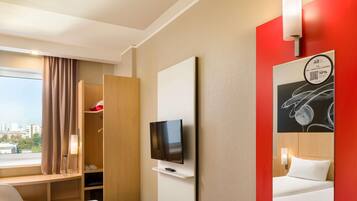 Une chambre d’hôtel avec deux lits, une télévision, une armoire et une fenêtre avec des rideaux.